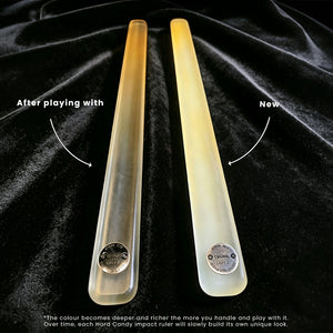 Two translucent hard candy impact rulers on a black velvet background, with text labels 'After playing with' and 'Now' showing color change over time. The left ruler is clear, and the right ruler is yellowed due to handling and play.