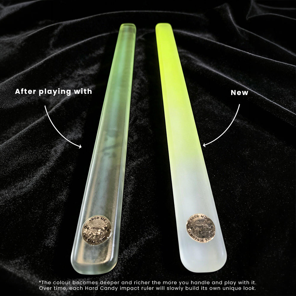 Two translucent hard candy impact rulers are displayed on a black velvet background, one labeled 'After playing with' showing a deeper green tint, and the other labeled 'New' showing a pale yellow-green tint. Both rulers have a coin embedded at the bottom.